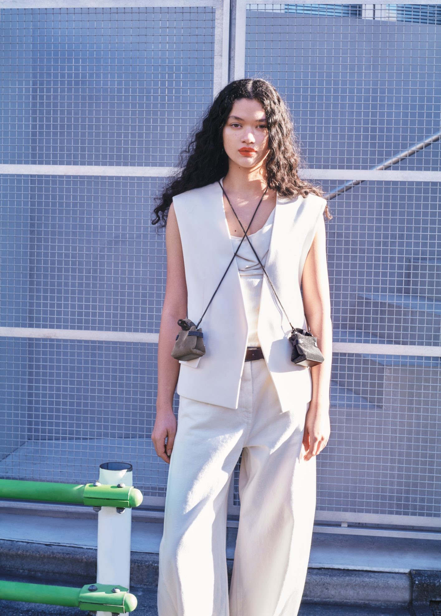 ブランドを象徴する「モニーレ」（極小のボールチェーン）を全面に配したデザインと、ベルベットを思わせるなめらかなスウェードの二つのバッグをレイヤード。バッグとしてはもちろん、チャームとしても活躍するミクロサイズは、〈Essence〉の新たな楽しみ方を教えてくれる。ブラックバッグ〈Micro Essence〉 H7.5×W8.5×D5.5cm ¥385,000、ベージュバッグ〈Micro Essence〉H7.5×W8.5×D5.5cm ¥235,400、ベスト ¥578,600、中に着たトップ ¥257,400、パンツ ¥271,700、ベルト ¥167,200（以上ブルネロ クチネリ | ブルネロ クチネリ ジャパン）