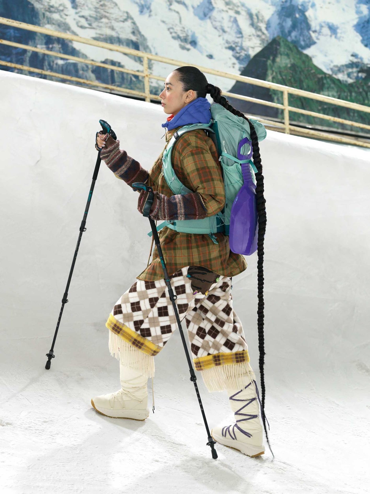タータンチェック柄やボーダー、アーガイル模様など、同系色のテキスタイルを大胆にミックス。背負ったソリと同じ紫をフードや靴紐など随所にちりばめてアクセントに。ジャケット ¥59,400(スドーク)、パンツ ¥95,700(ペナルティメイト | 共にエムエイティティ)/中に着たダウン ¥25,3 00(マーモット | サードシップ)/中に着たタートルネック ¥20,900(スノーピーク)/バックパック ¥26,400(ミレー | ミレー・マウンテン・グループ・ジャパン・カスタマーサービス)/アームウォーマー ¥24,200(セヴシグ | サカス ピーアール)/スノーブーツ ¥39,600(ハンター | ハンタージャパン カスタマーサービス)/トレッキングポール*スタイリスト私物